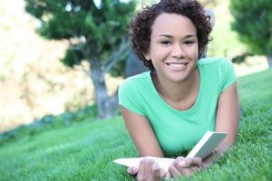Girl laying in the grass with a book smiling at the camera